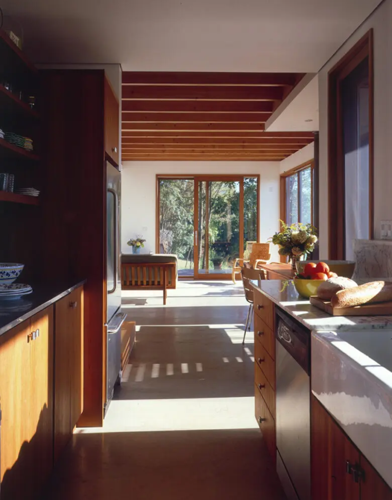 A kitchen with wooden cabinets and floors, and a large window.