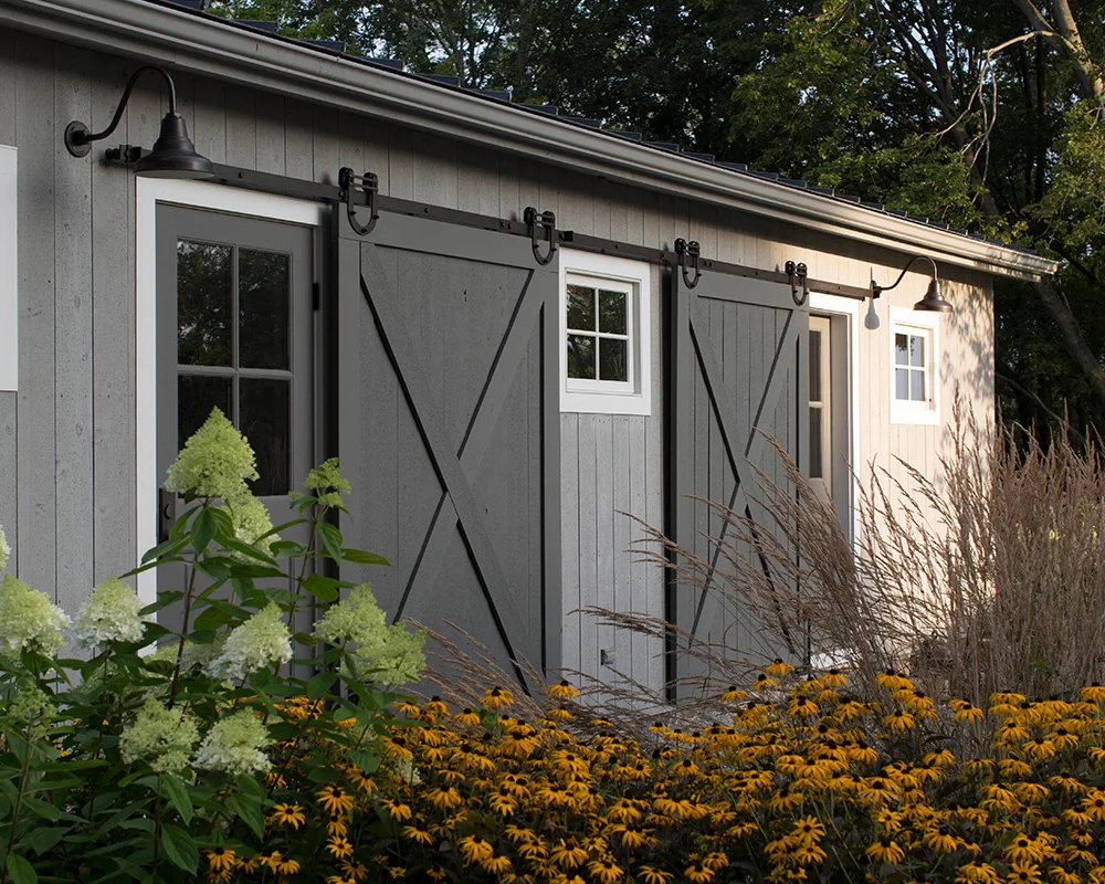 A barn with two doors and flowers in the foreground.