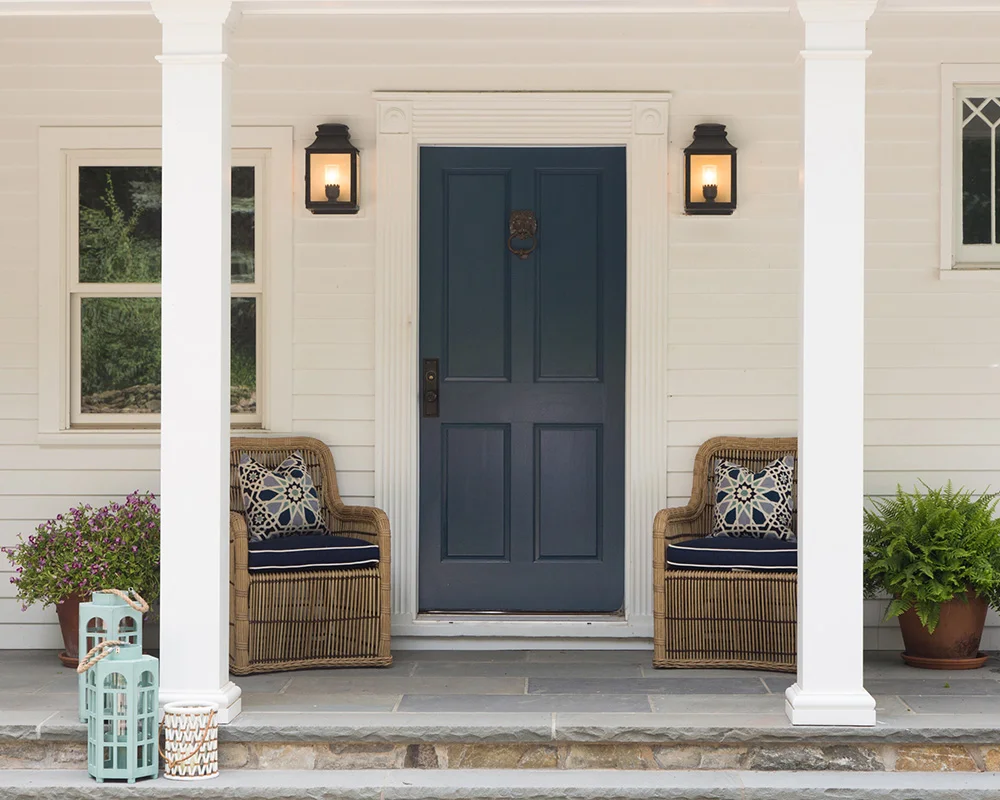 A front porch with two chairs and a blue door.